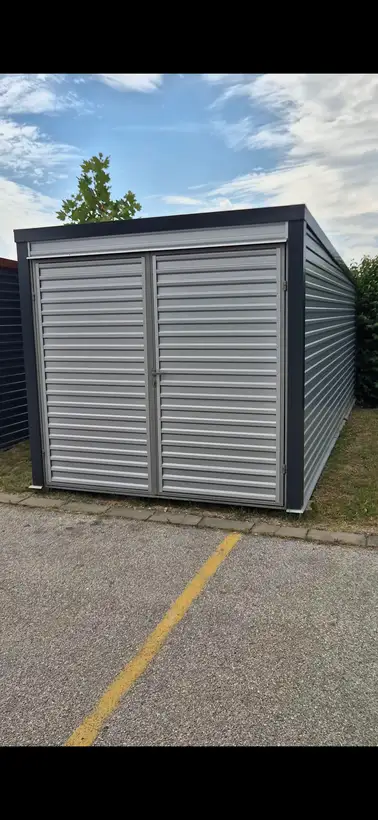 Antracit garaža sa svetlim vratima pod vedrim nebom
